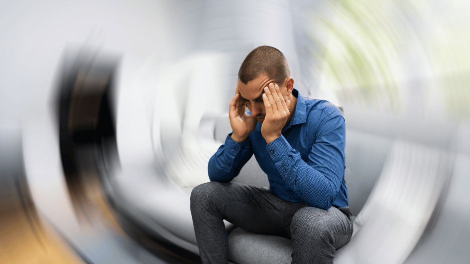 A man experiencing vertigo with a blurred spinning background, depicting the disorienting effects of vertigo as he holds his head in discomfort