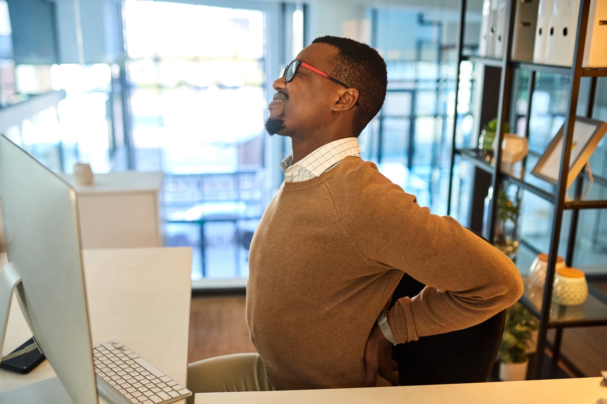 Man sitting at desk suffering from back spasms. 