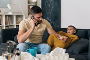 Father checking his child's temperature on a thermometer while on the phone with a doctor about communicable illnesses