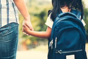  Child wearing a backpack holding parent's hand, returning to school after the COVID-19 pandemic