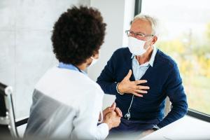 Patient in mask describing panic attack vs. heart attack symptoms to a medical professional