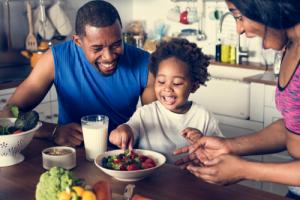 Two parents smiling as their young daughter eats strawberries from a bowl