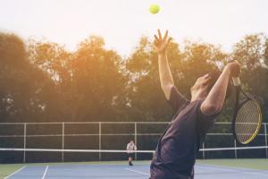 A man partaking in the physical activity pyramid by serving up a tennis ball to a friend