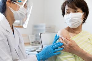 Doctor wearing PPE administering a COVID-19 Booster to an at-risk patient