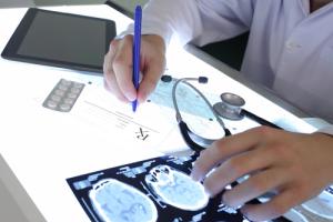 Closeup of a doctor outlining the effects of epilepsy after studying brain scans on a desk