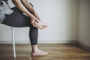 Woman sitting in chair massages her foot after experiencing common sports injuries