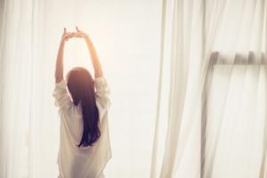 Woman sitting in front of a window, stretching arms high above her head after using her CPAP Machine