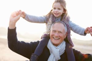 Elderly man carrying a young girl on his shoulders after looking after his heart health