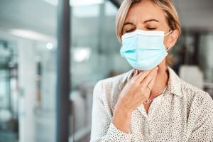 Masked woman massages her neck after experiencing oral cancer symptoms