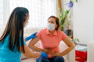 Masked woman with hands over her abdomen displaying gallbladder disease symptoms to her doctor