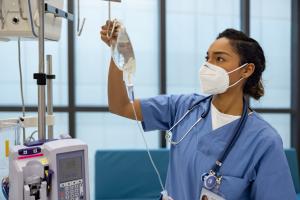 Masked doctor checking IV bag during a cancer therapy session