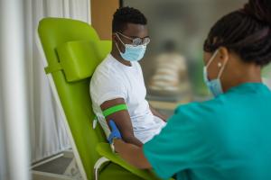 Masked man receiving a blood transfusion from a nurse