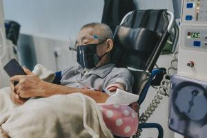 Masked patient looking at his phone while undergoing the kidney dialysis process