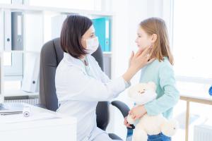 Masked doctor examining a young patient for infectious mononucleosis symptoms through swollen lymph nodes