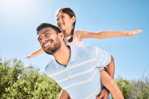 Father carrying daughter on his back on a sunny day