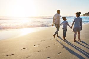 Father, mother, and child walking along a beach during safe summer travel