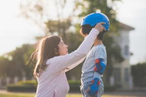 Woman putting a blue helmet on her child, practicing summer safety tips for kids