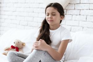 Young girl grasping her knee after experiencing severe juvenile arthritis symptoms