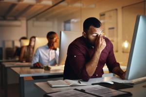 Man in class rubbing his eyes at computer after experiencing poor eye health