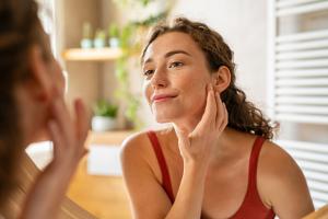 Woman smiling in the mirror examining her face for skin tags