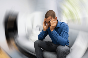A man experiencing vertigo with a blurred spinning background, depicting the disorienting effects of vertigo as he holds his head in discomfort